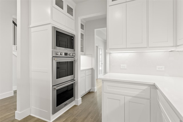 kitchen with built in microwave, light wood-style flooring, stainless steel double oven, white cabinets, and backsplash