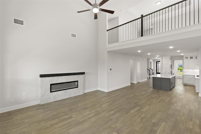 unfurnished living room featuring a glass covered fireplace, baseboards, a ceiling fan, and visible vents