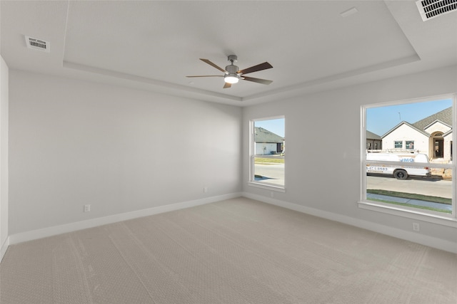 unfurnished room featuring visible vents, a raised ceiling, ceiling fan, and light carpet