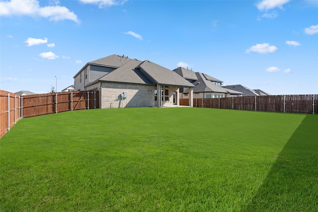 rear view of house with brick siding, roof with shingles, a lawn, and a fenced backyard