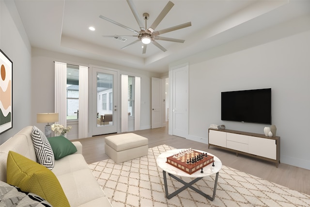 living room with a raised ceiling, ceiling fan, and light hardwood / wood-style flooring