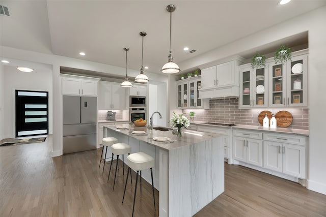 kitchen featuring built in appliances, backsplash, white cabinets, and an island with sink