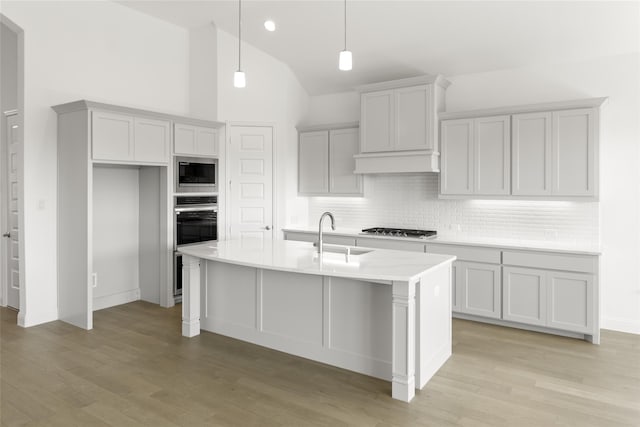 kitchen with light hardwood / wood-style flooring, appliances with stainless steel finishes, pendant lighting, and a kitchen island with sink