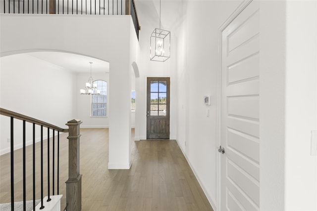 foyer with wood-type flooring, ornamental molding, an inviting chandelier, and a high ceiling