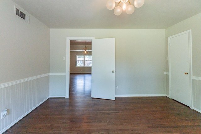 empty room featuring dark wood-type flooring and a notable chandelier