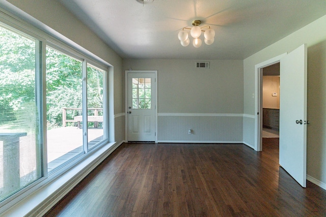 spare room featuring dark wood-type flooring and a chandelier