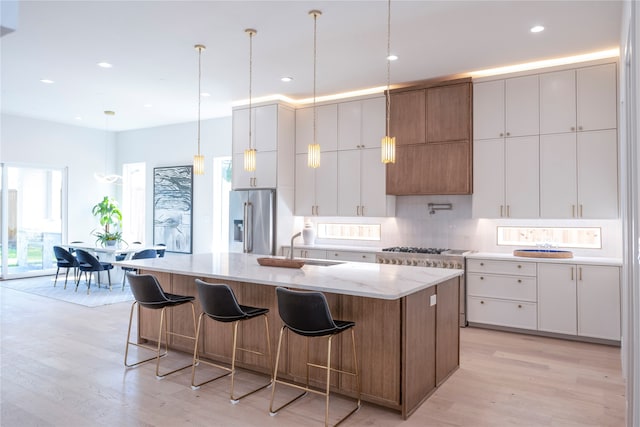 kitchen featuring high end refrigerator, white cabinetry, an island with sink, and light hardwood / wood-style floors