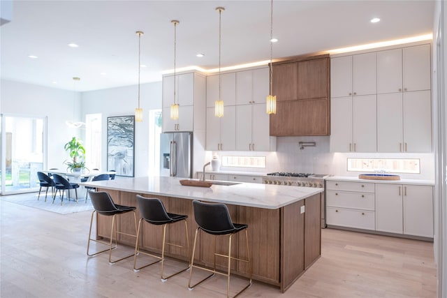 kitchen with high end fridge, light hardwood / wood-style flooring, pendant lighting, a kitchen island with sink, and white cabinets