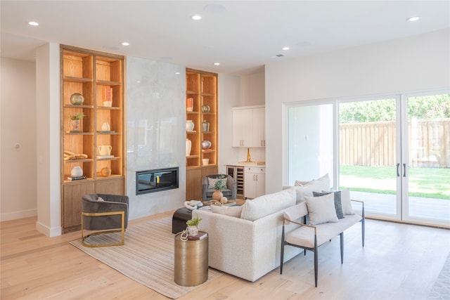 living room with built in features, a high end fireplace, beverage cooler, and light wood-type flooring