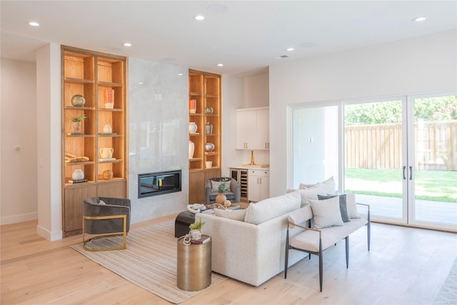 living room with a high end fireplace, light hardwood / wood-style flooring, built in features, and a wealth of natural light