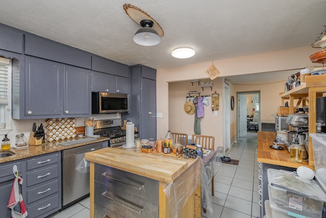 kitchen with butcher block countertops, tasteful backsplash, appliances with stainless steel finishes, and light tile patterned floors