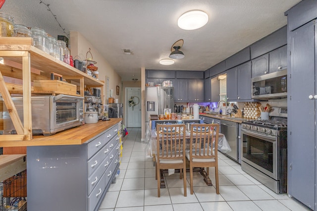 kitchen featuring gray cabinets, stainless steel appliances, sink, butcher block countertops, and light tile patterned floors