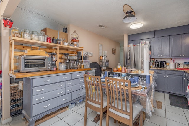 kitchen with gray cabinets, light tile patterned floors, a kitchen island, a textured ceiling, and stainless steel fridge with ice dispenser