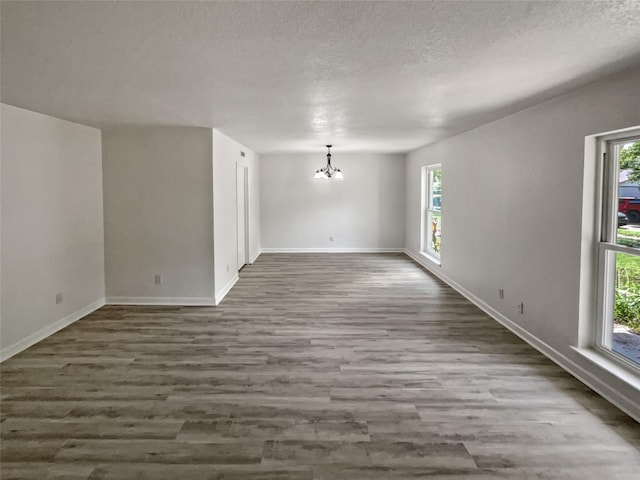 unfurnished room with a textured ceiling, an inviting chandelier, and dark hardwood / wood-style floors