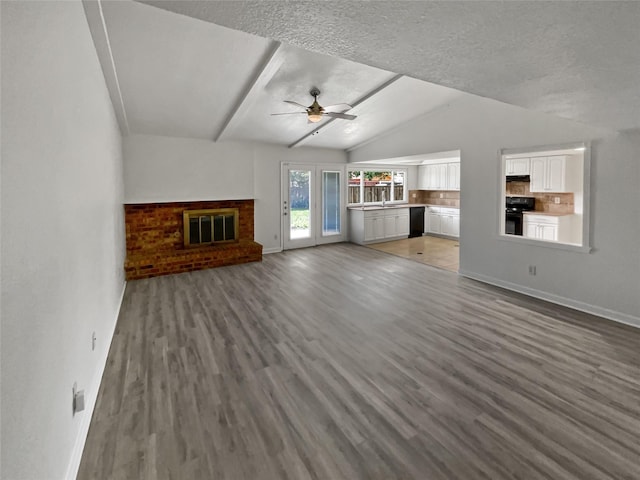 unfurnished living room with a textured ceiling, vaulted ceiling, hardwood / wood-style floors, a fireplace, and ceiling fan