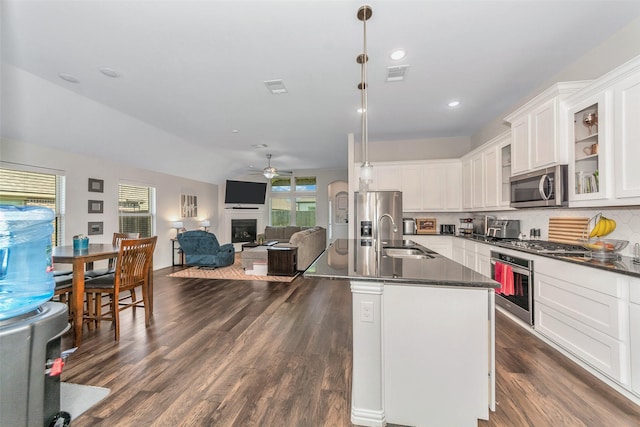 kitchen with white cabinetry, hanging light fixtures, stainless steel appliances, tasteful backsplash, and an island with sink