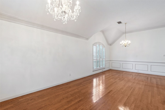 empty room featuring an inviting chandelier, wood-type flooring, ornamental molding, and vaulted ceiling