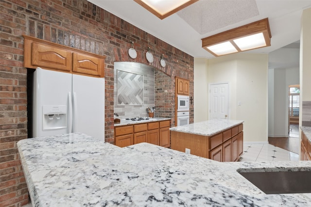 kitchen with light stone counters, brick wall, white appliances, a kitchen island, and light tile patterned flooring