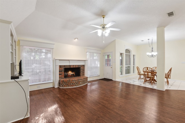 unfurnished living room with a healthy amount of sunlight, a brick fireplace, hardwood / wood-style floors, vaulted ceiling, and ceiling fan with notable chandelier