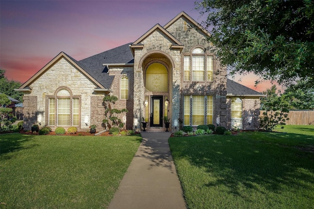 french provincial home with brick siding, a lawn, and a shingled roof