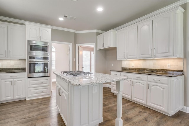 kitchen featuring white cabinets, dark stone counters, wood finished floors, a center island, and stainless steel appliances