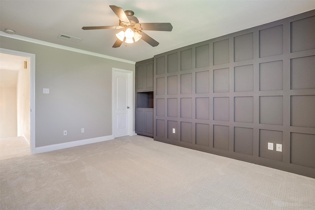 unfurnished bedroom with light colored carpet, a decorative wall, visible vents, baseboards, and ornamental molding