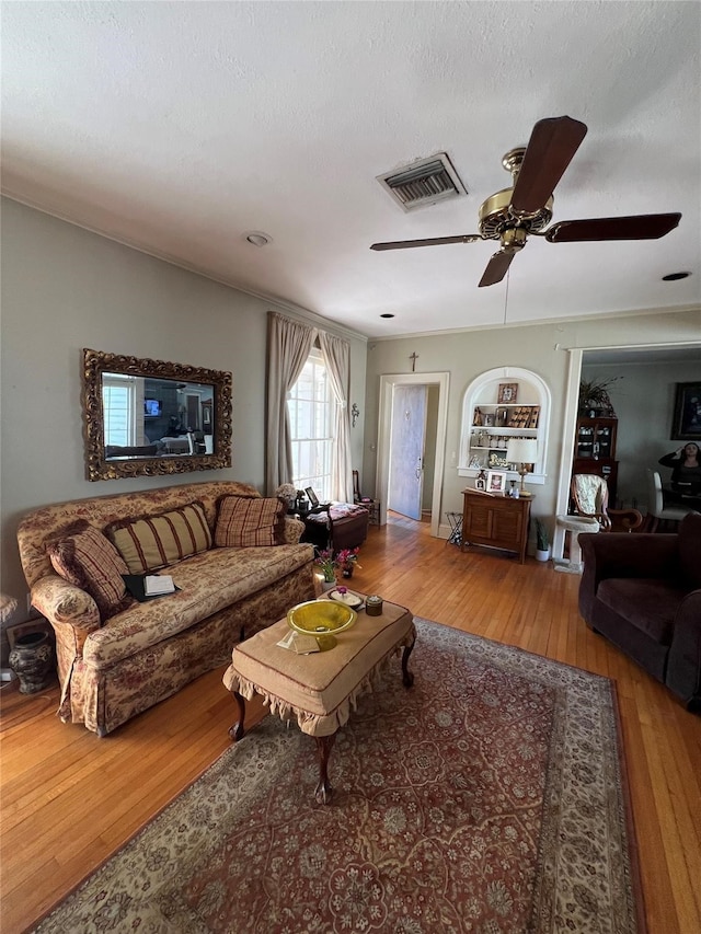 living room with built in shelves, ceiling fan, hardwood / wood-style flooring, and a textured ceiling