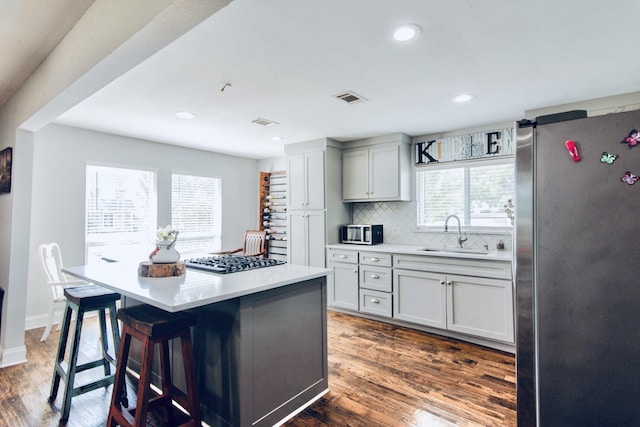 kitchen with stainless steel appliances, dark wood-type flooring, sink, a kitchen island, and a breakfast bar area