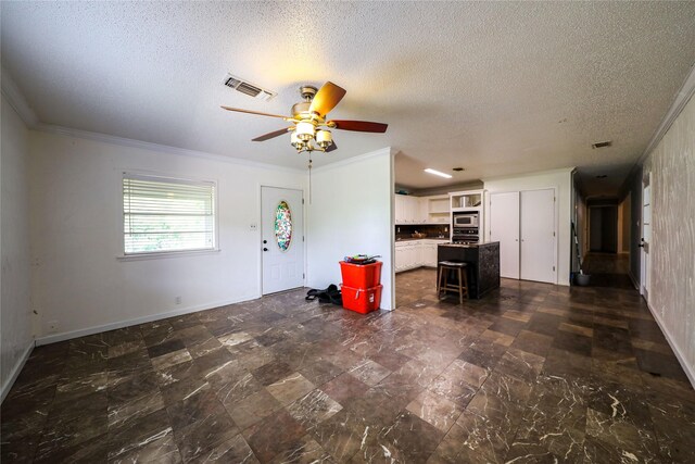 unfurnished living room featuring ceiling fan, a textured ceiling, dark tile floors, and ornamental molding