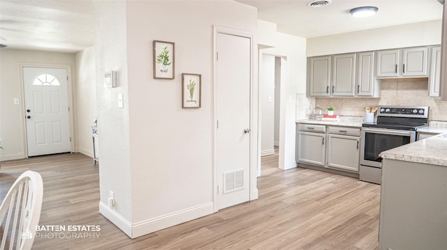 kitchen with gray cabinetry, decorative backsplash, stainless steel electric stove, and light hardwood / wood-style floors