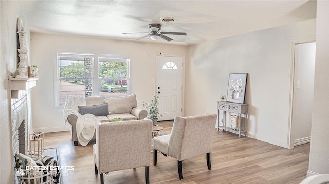 living room featuring a brick fireplace, light hardwood / wood-style flooring, and ceiling fan