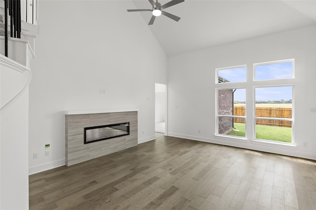 unfurnished living room featuring dark wood-type flooring, ceiling fan, a tiled fireplace, and high vaulted ceiling