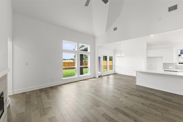 unfurnished living room with high vaulted ceiling, ceiling fan with notable chandelier, and dark hardwood / wood-style floors