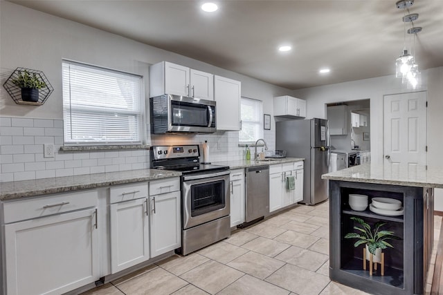 kitchen with white cabinetry, appliances with stainless steel finishes, washer and clothes dryer, and light stone counters