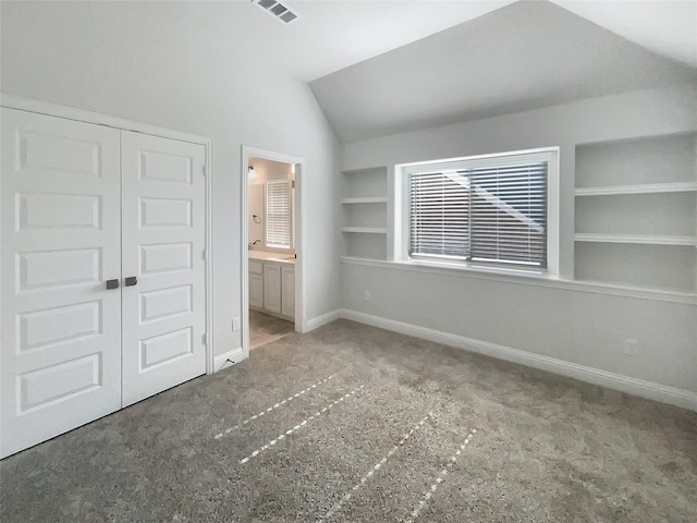 unfurnished bedroom featuring ensuite bathroom, a closet, vaulted ceiling, and carpet floors