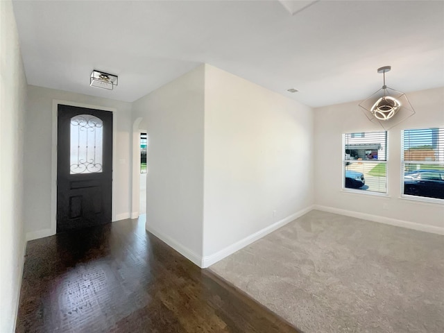 entrance foyer featuring a notable chandelier, a wealth of natural light, and dark colored carpet