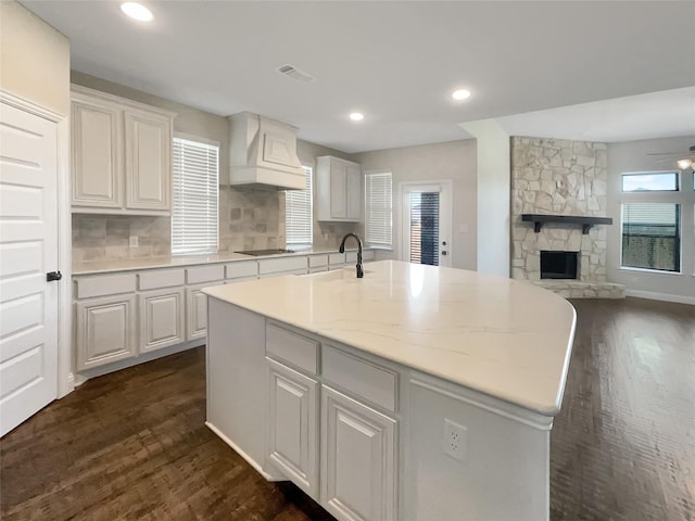 kitchen featuring white cabinets, custom exhaust hood, an island with sink, and sink