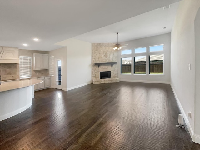 unfurnished living room with ceiling fan, dark hardwood / wood-style flooring, and a stone fireplace