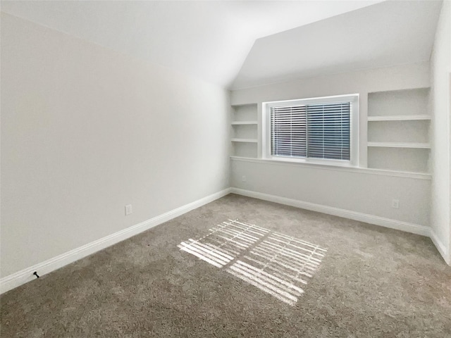 carpeted empty room with built in shelves and vaulted ceiling