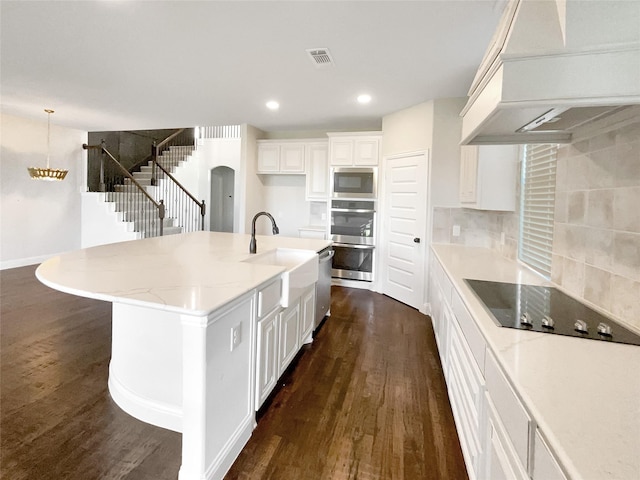 kitchen featuring appliances with stainless steel finishes, custom range hood, white cabinets, and an island with sink