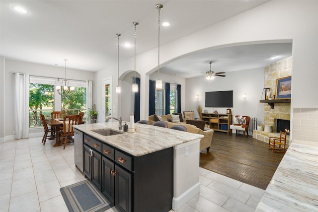 kitchen featuring arched walkways, dishwasher, a fireplace, a sink, and light tile patterned flooring