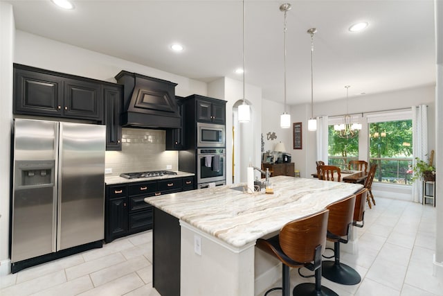 kitchen with dark cabinets, stainless steel appliances, premium range hood, a sink, and decorative backsplash