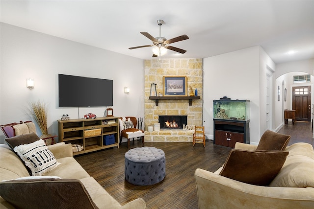 living room featuring arched walkways, ceiling fan, a stone fireplace, and wood finished floors