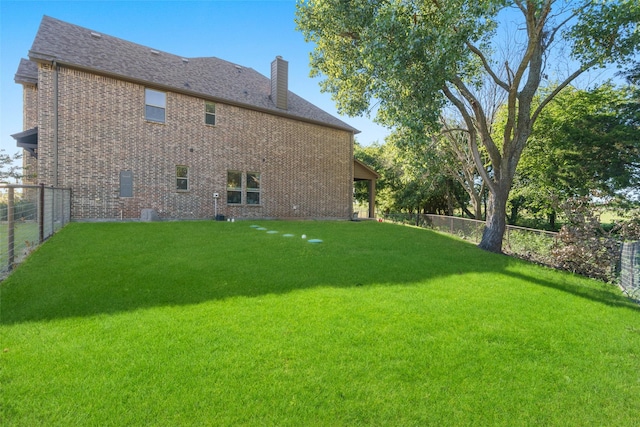 rear view of property featuring brick siding, a fenced backyard, a chimney, and a yard