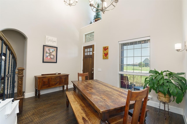 dining space with arched walkways, a notable chandelier, a towering ceiling, dark wood-type flooring, and baseboards