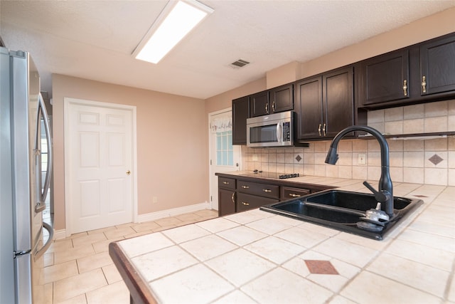 kitchen with tile countertops, backsplash, sink, dark brown cabinetry, and stainless steel appliances