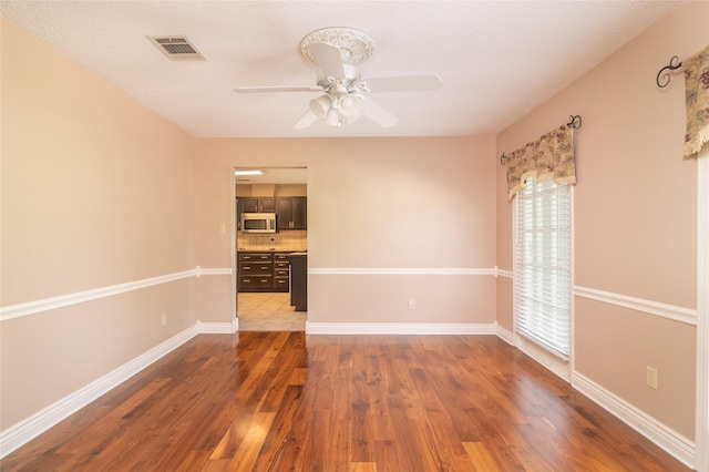 spare room with a textured ceiling, ceiling fan, and dark wood-type flooring