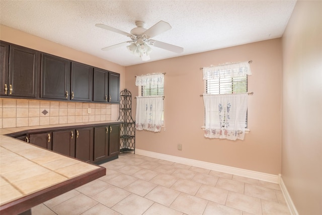 kitchen with a textured ceiling, dark brown cabinets, and backsplash