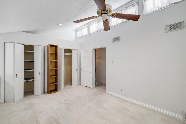 unfurnished bedroom with ceiling fan, high vaulted ceiling, light colored carpet, and two closets