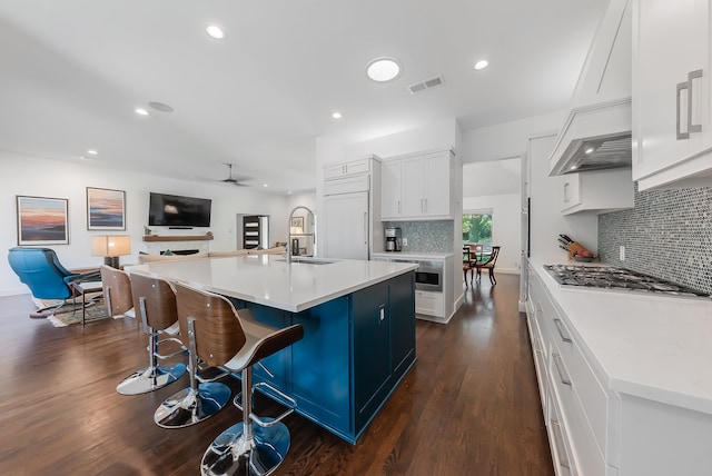 kitchen featuring white cabinetry, sink, stainless steel appliances, dark wood-type flooring, and a center island with sink